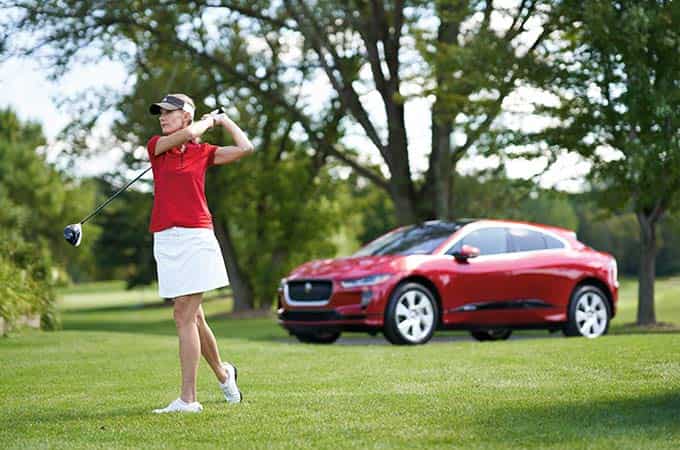 Donna practicing on the golf course with her I-PACE parked nearby.