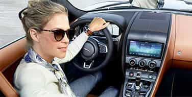 Woman wearing sunglasses at the wheel of a Jaguar F-TYPE Convertible.