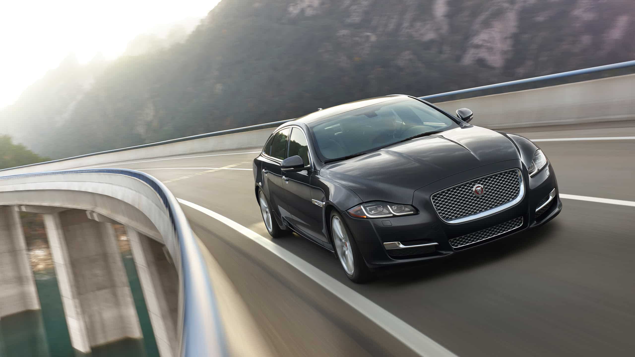 Jaguar XJ running on the bridge which is build over the river and surrounded by mountains